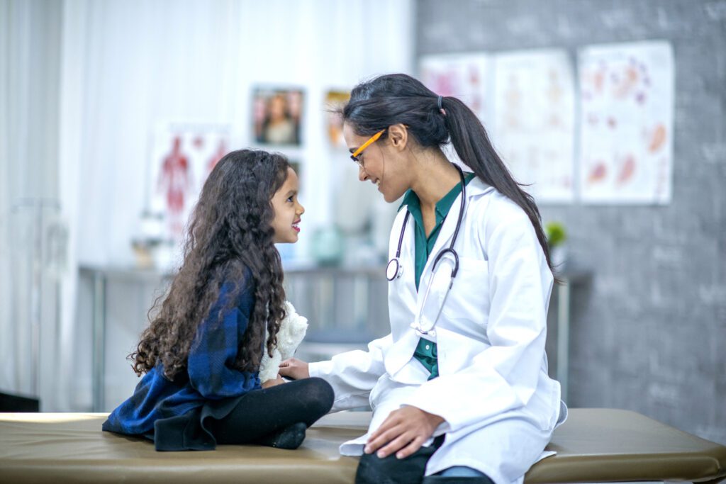 Female doctor smiling at a young girl holding a stuffed toy during a medical exam