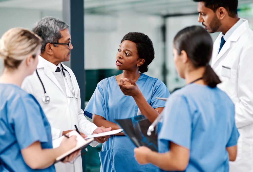 Three doctors taking notes while a trainee talks with a senior doctor