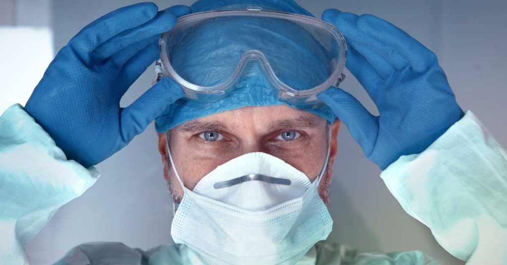 A surgeon wearing a surgical mask pulling down his goggles