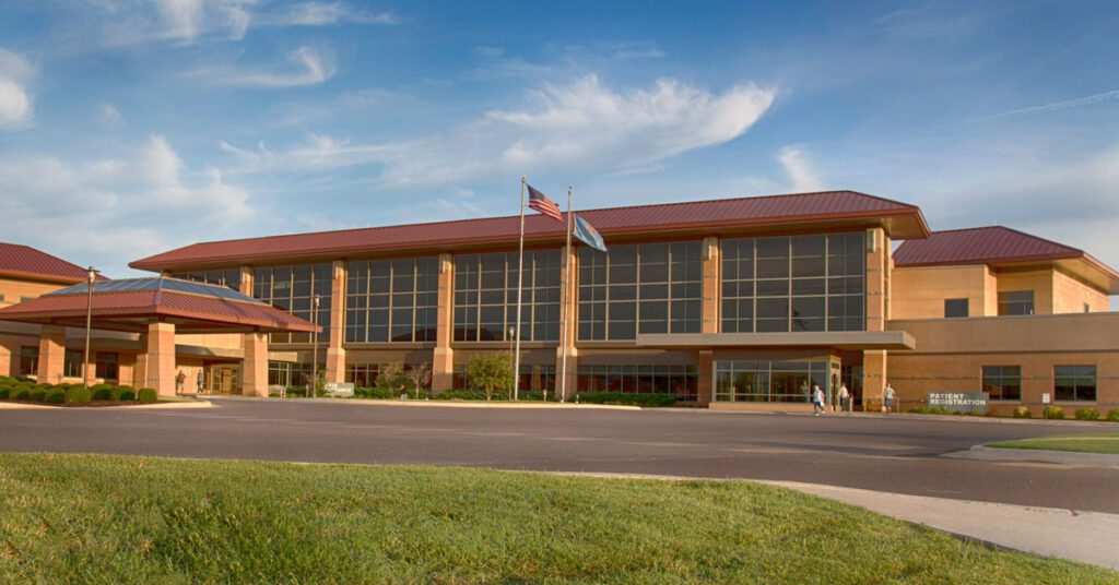 Exterior view of a medical center building with a red roof, large glass windows, and flagpoles in front