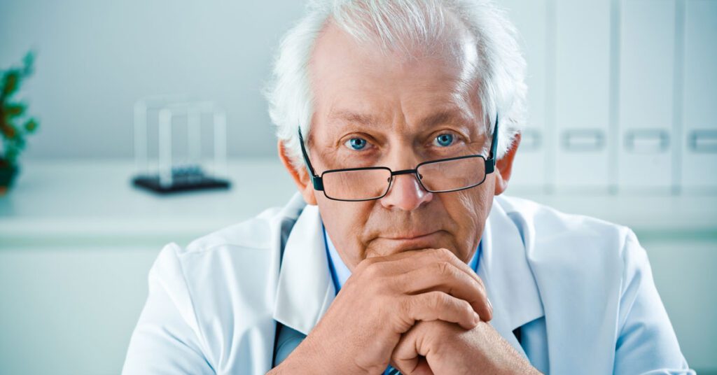 Senior male doctor with glasses, resting his chin on his hands