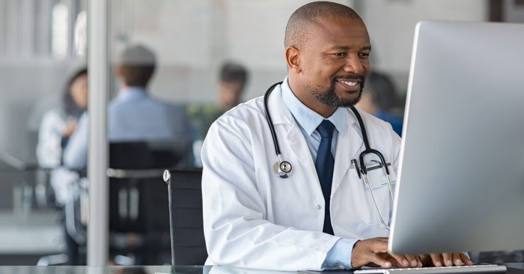 Doctor smiling while using a computer while other doctors talking in background