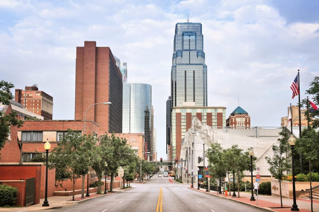 View of a city street lined with trees, leading toward tall buildings and skyscrapers