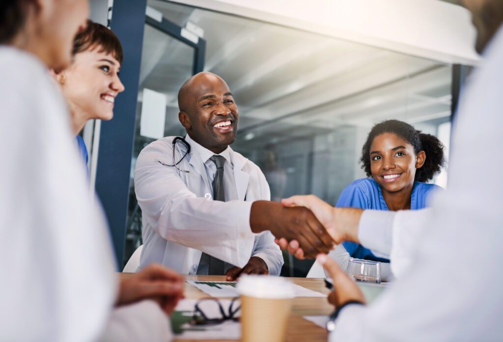 Doctors smiling and shaking hands during a meeting, showing teamwork