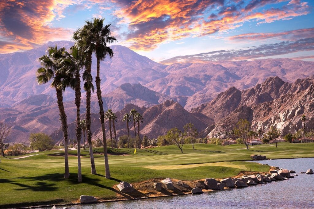 Palm trees on a golf course with mountains in front of a colorful sunset