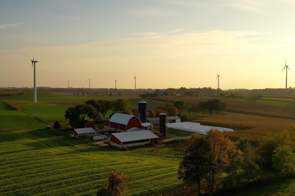 A farm with red barns, silos, and wind turbines in the background