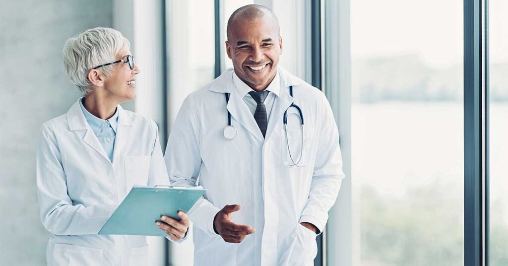 Smiling male and female doctors talking, with the female doctor holding a writing pad