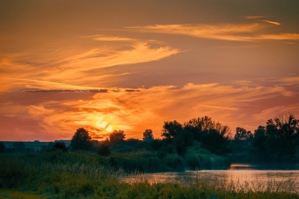 Stunning sunset over a serene river with silhouettes of trees and vibrant clouds