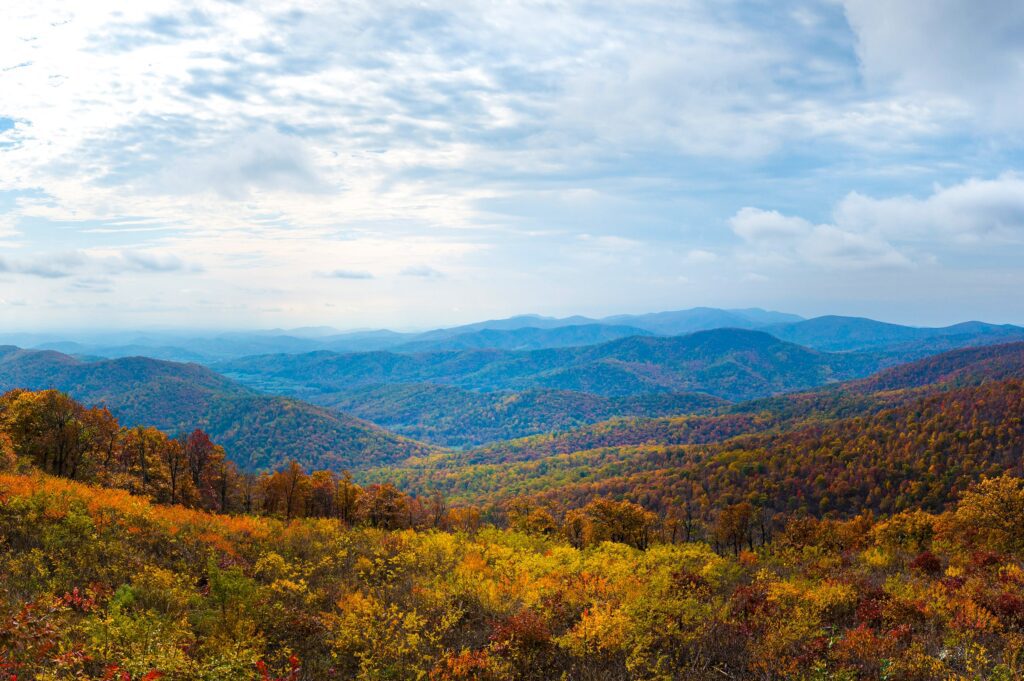 Expansive view of a mountain range covered in vibrant autumn foliage under a cloudy sky