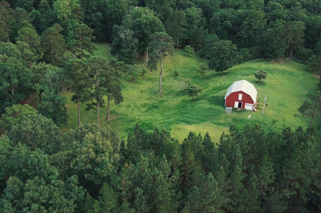 Aerial view of a red barn surrounded by lush green trees and grass on a serene landscape