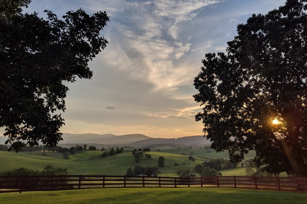 A sunset view of a valley with trees and mountains in the background