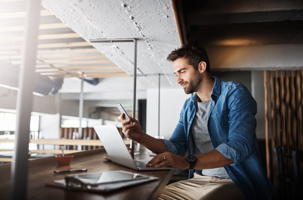 Man working on a laptop and looking at his phone