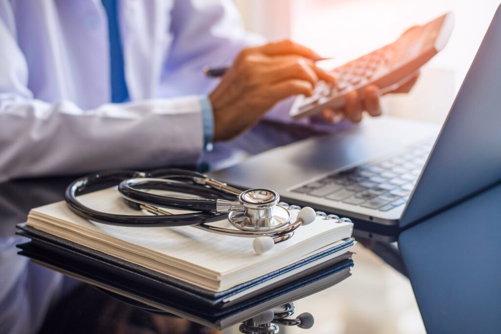 Doctor calculating medication dosage with a calculator beside a laptop and medical books