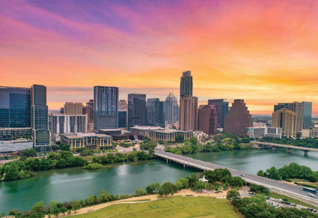 Vibrant city skyline with tall buildings and a river at sunset featuring orange and pink skies