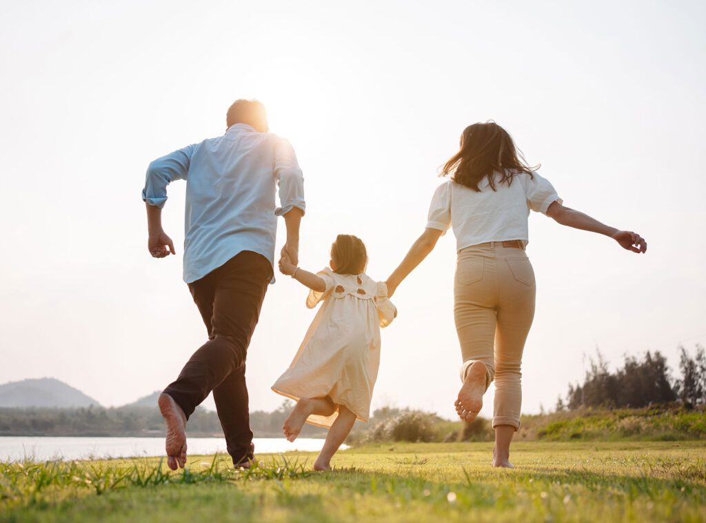 Happy family running together in a grassy field with the sun shining in the background