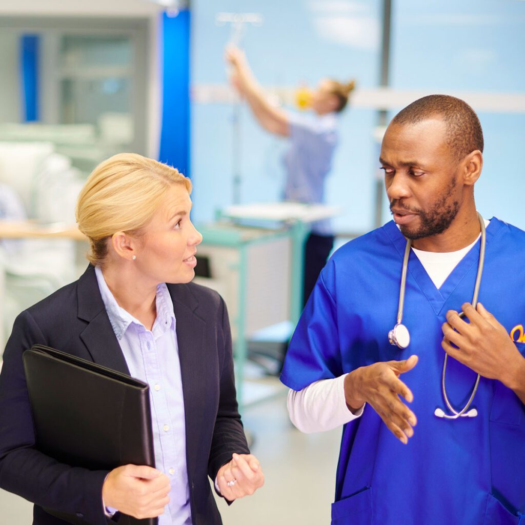 Medical professional in blue scrubs discussing with a businesswoman in a hospital setting