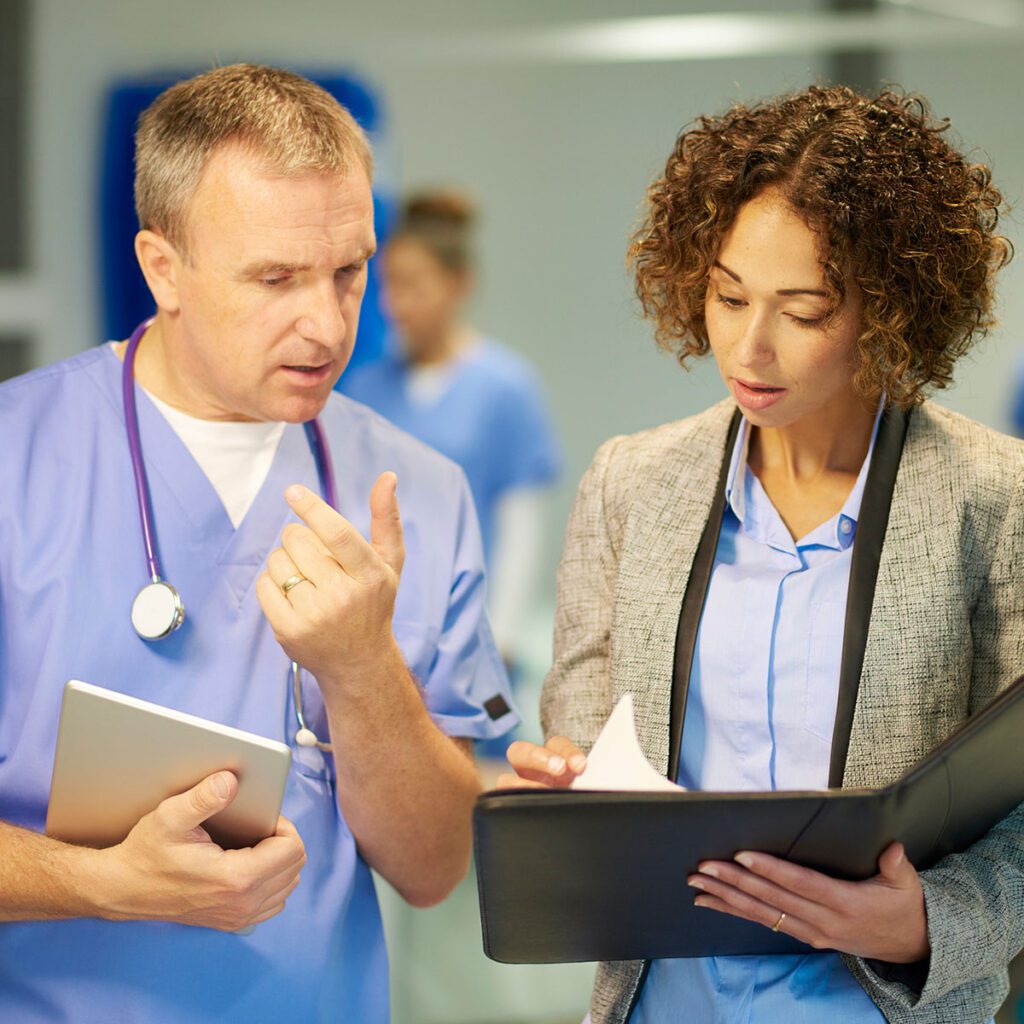 Doctor in blue scrubs explaining a report to a professional woman holding a file