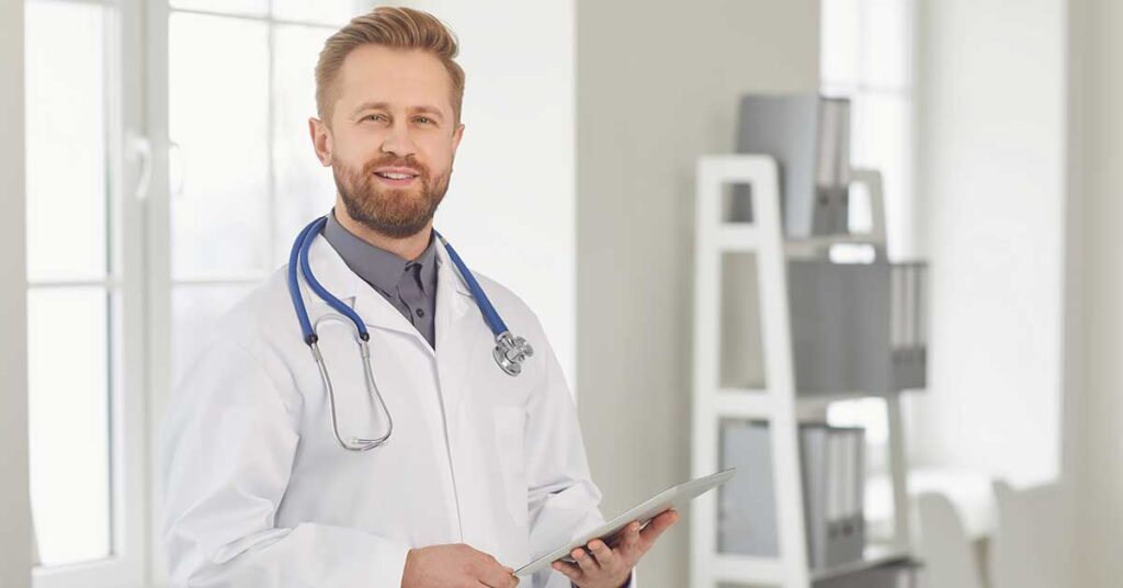 A doctor with a stethoscope around his neck is holding a tablet