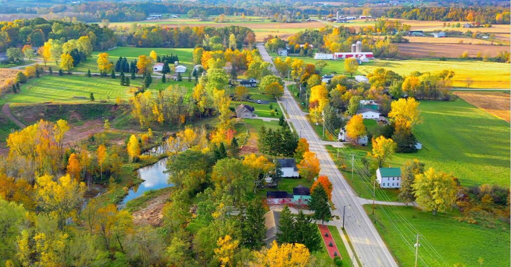 Aerial view of a rural landscape with vibrant fall colors, fields, and a winding road