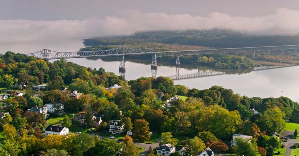 Aerial view of a scenic bridge over a river, surrounded by lush green trees and residential home