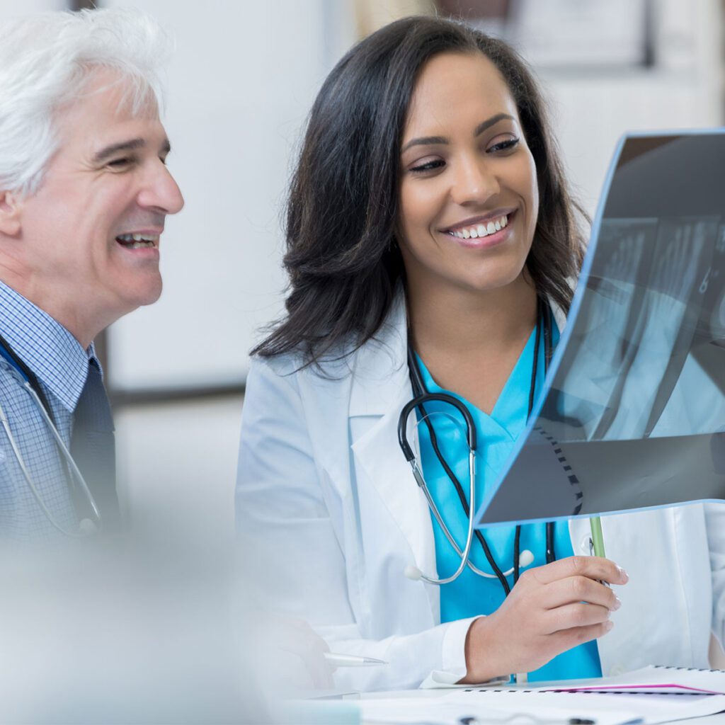 Female doctor reviewing an X-ray with a senior colleague, both smiling in a clinical setting